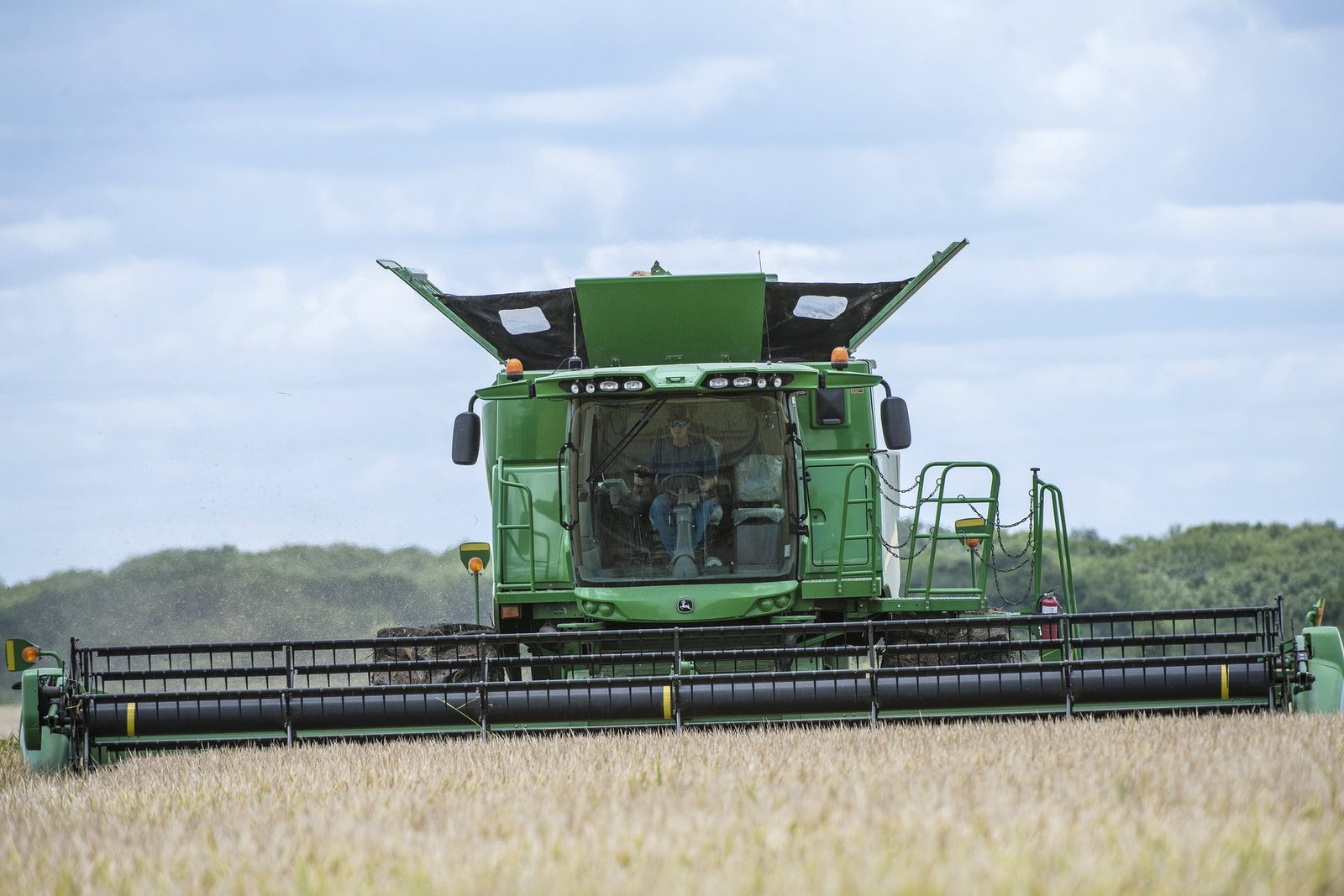 A green combine cutting a small grain field