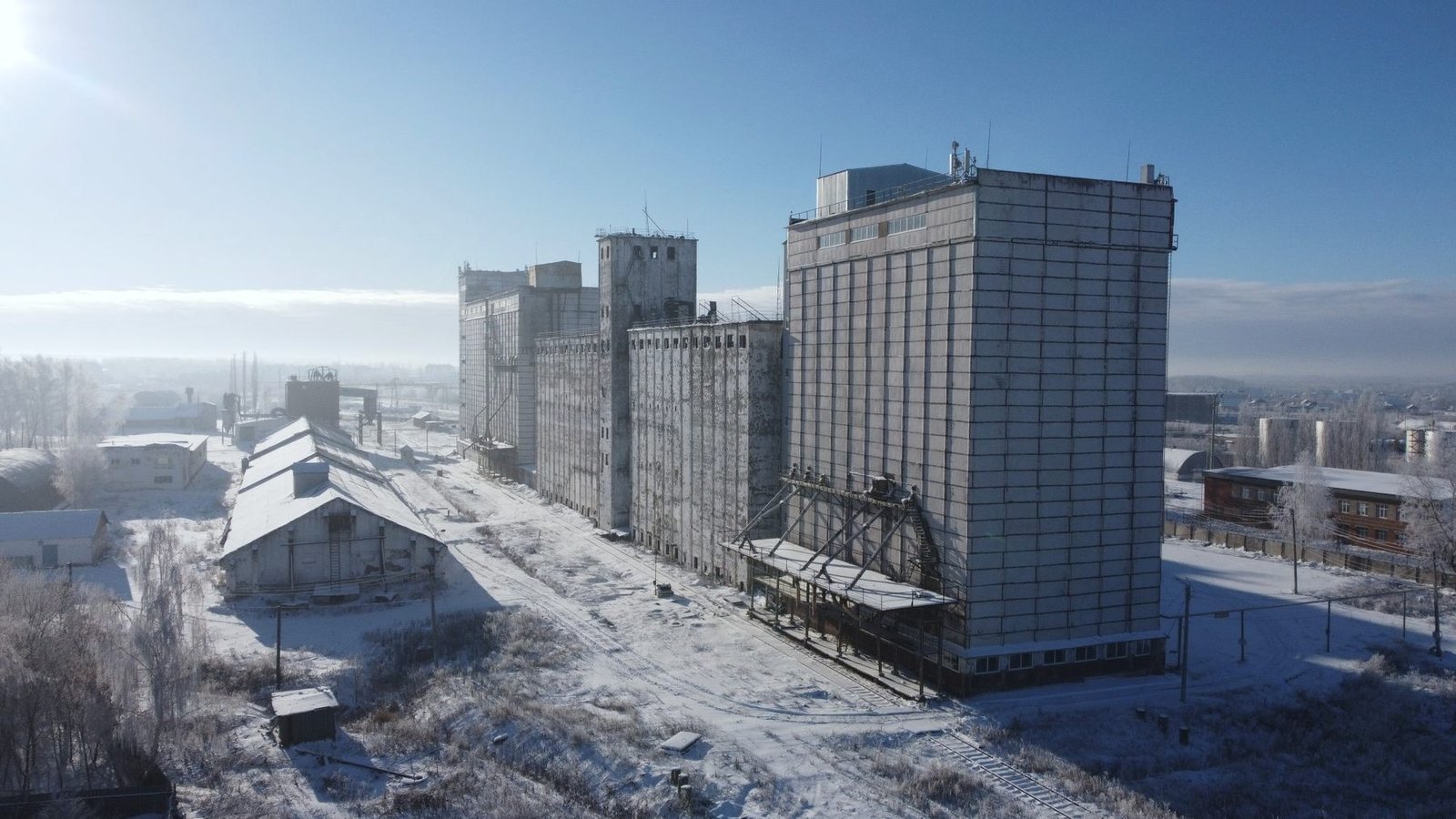 Concrete and steel grain elevators beside a snow-covered rail yard on a cold, clear morning